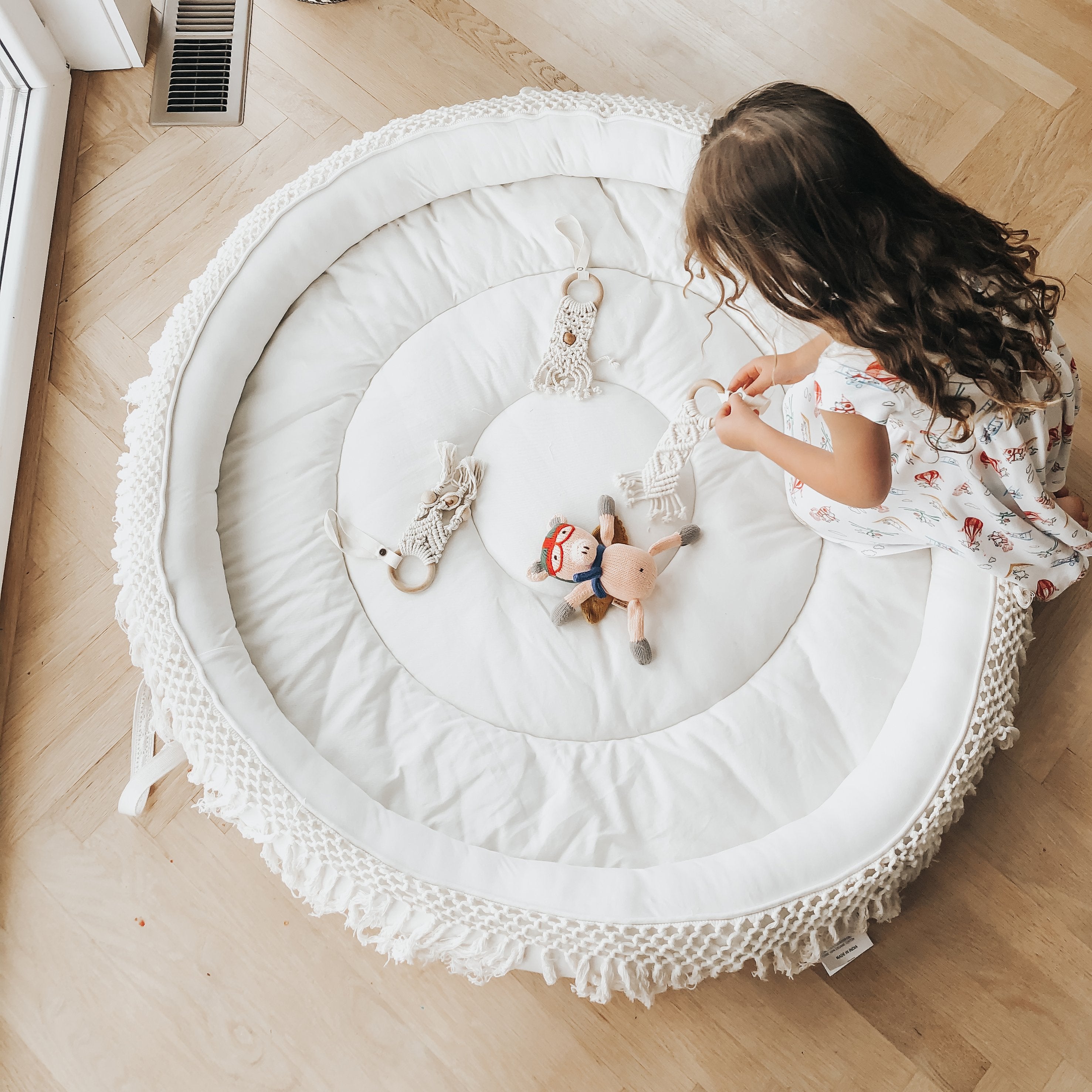 Child playing with toys on a round white mat in a room with wooden flooring. Main image