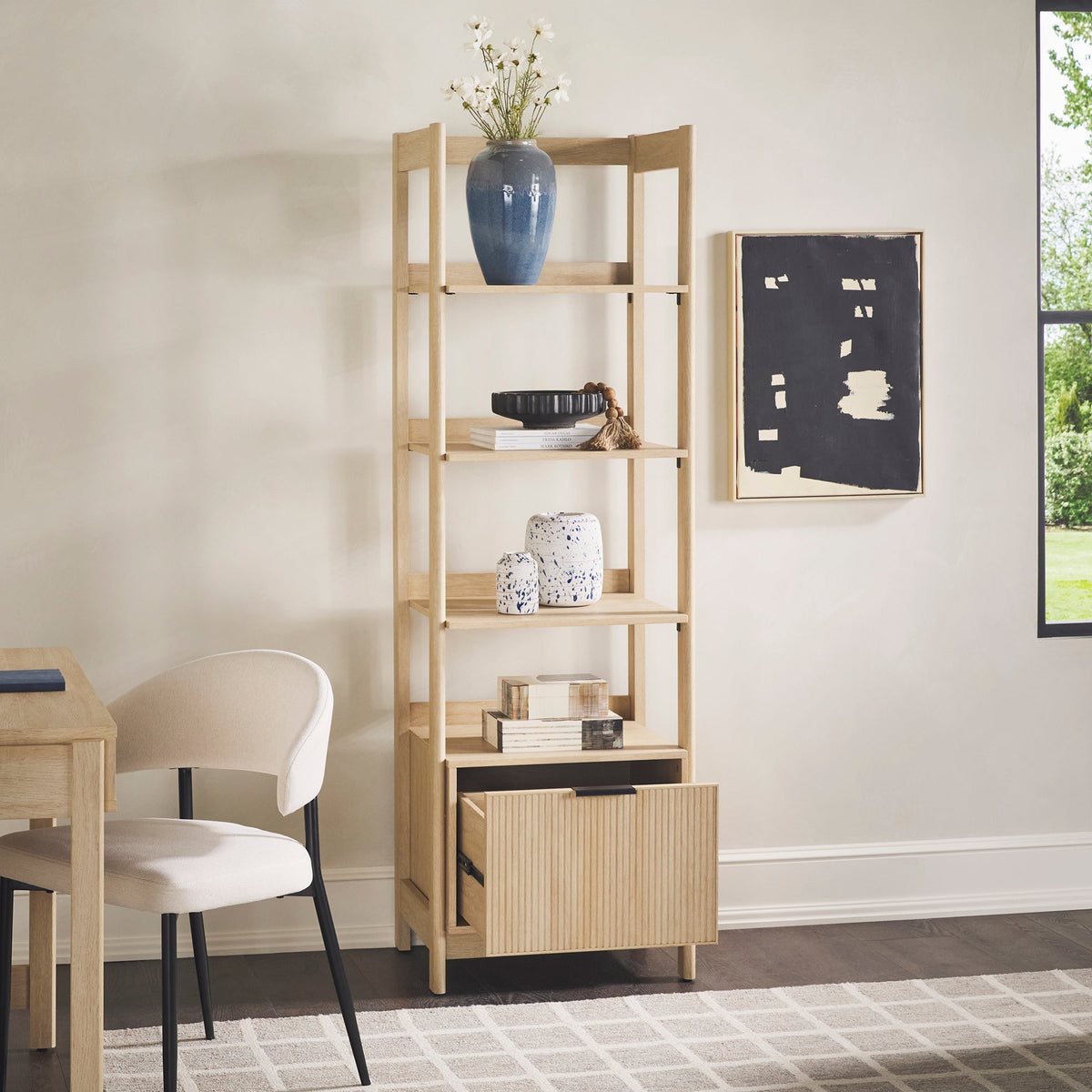 Light wooden bookshelf with decorative items in a room with a chair and table.