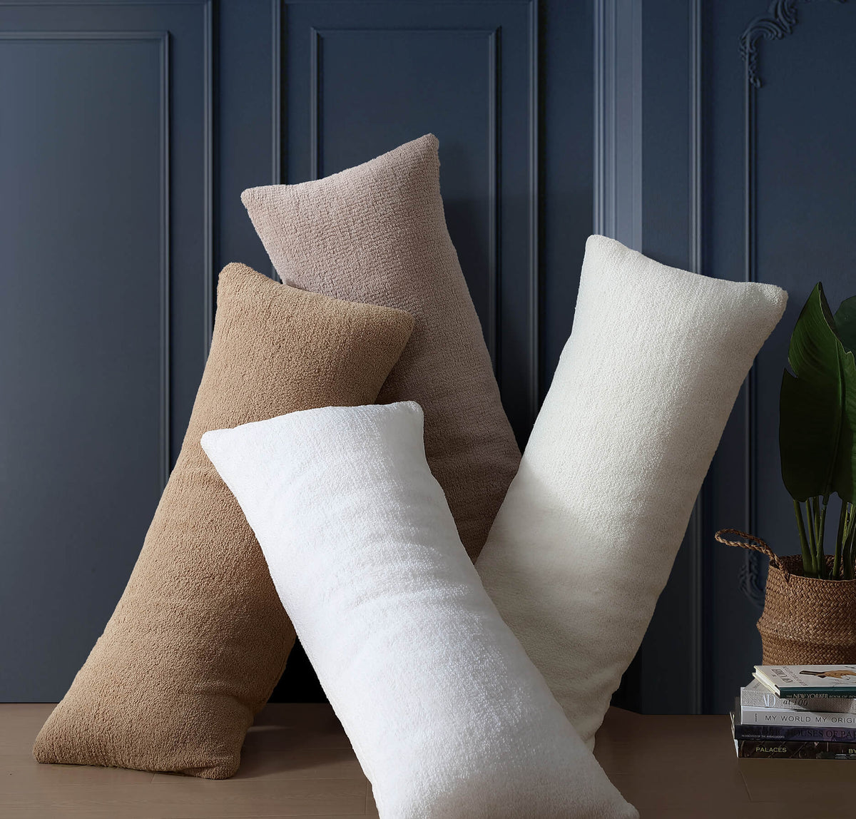 Four decorative pillows in beige, brown, and white against a dark blue paneled wall.