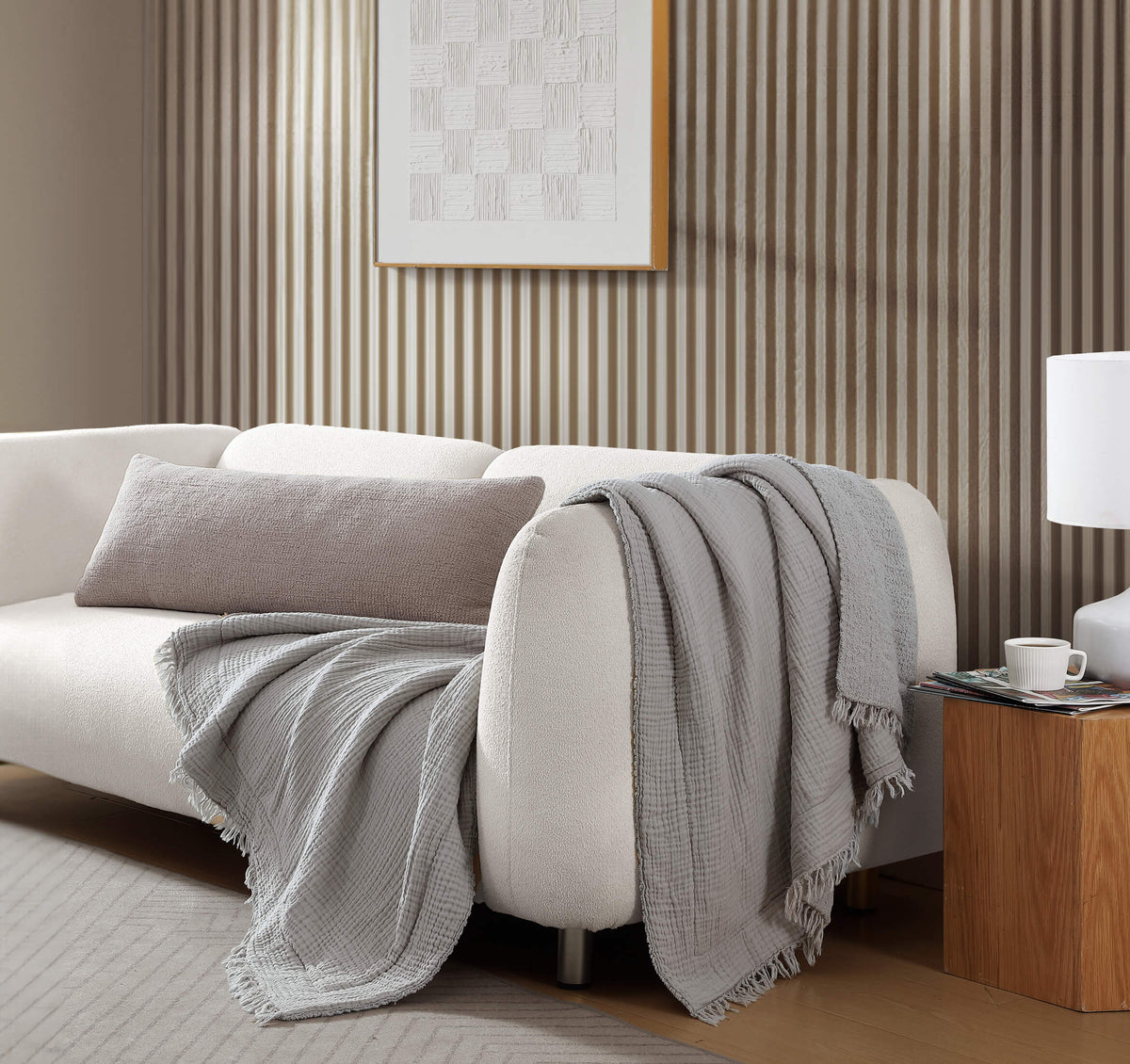 White sofa with gray throw blanket and pillow in a living room setting.