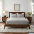 Wide-angle view of bedroom with feather gray bamboo sheets on walnut bed frame, featuring matching nightstand, ceramic lamp, glass vase with greenery, soft rug, and minimal wall art.