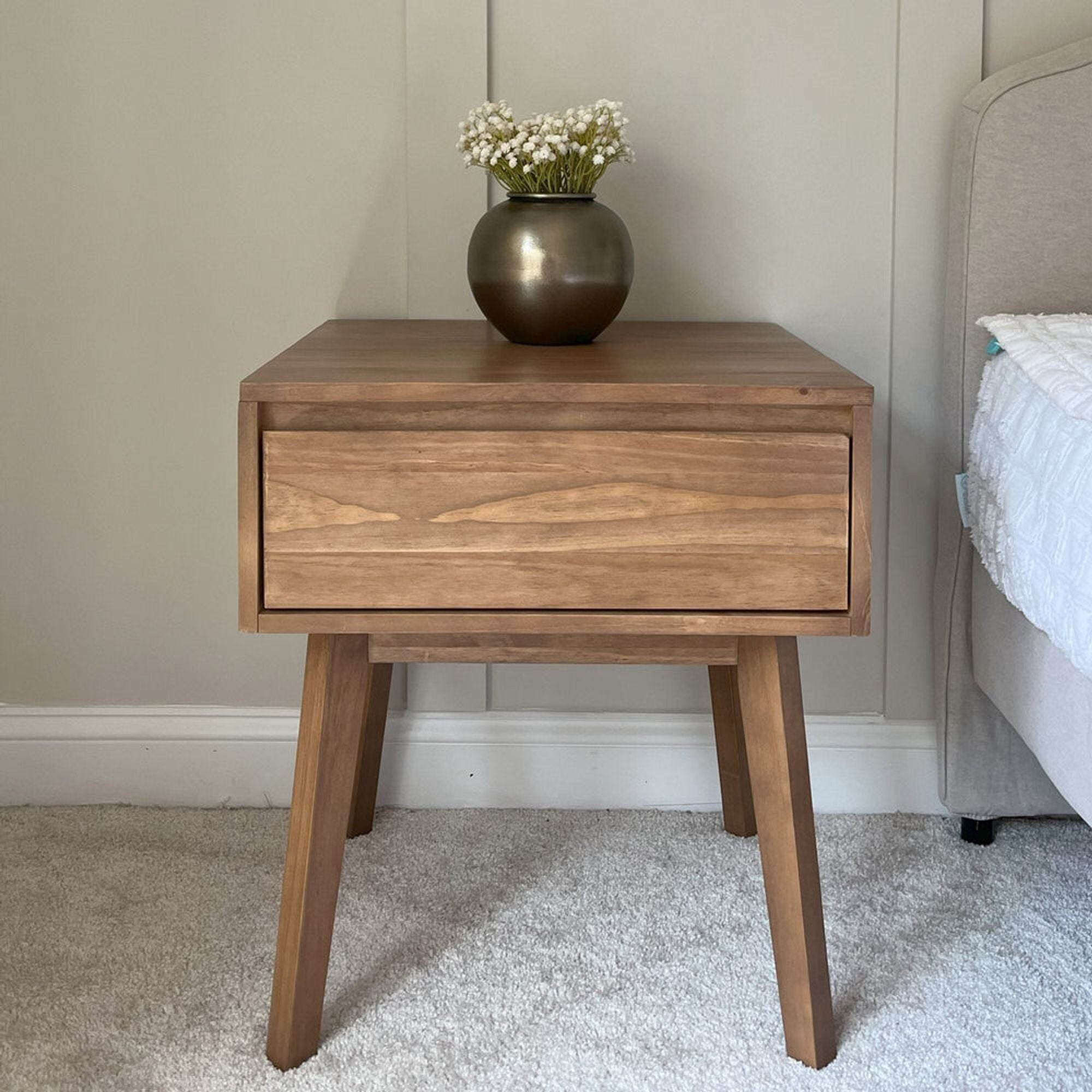 Mid-century modern wooden bedside table with a single drawer and a vase of white flowers placed on top. Main image