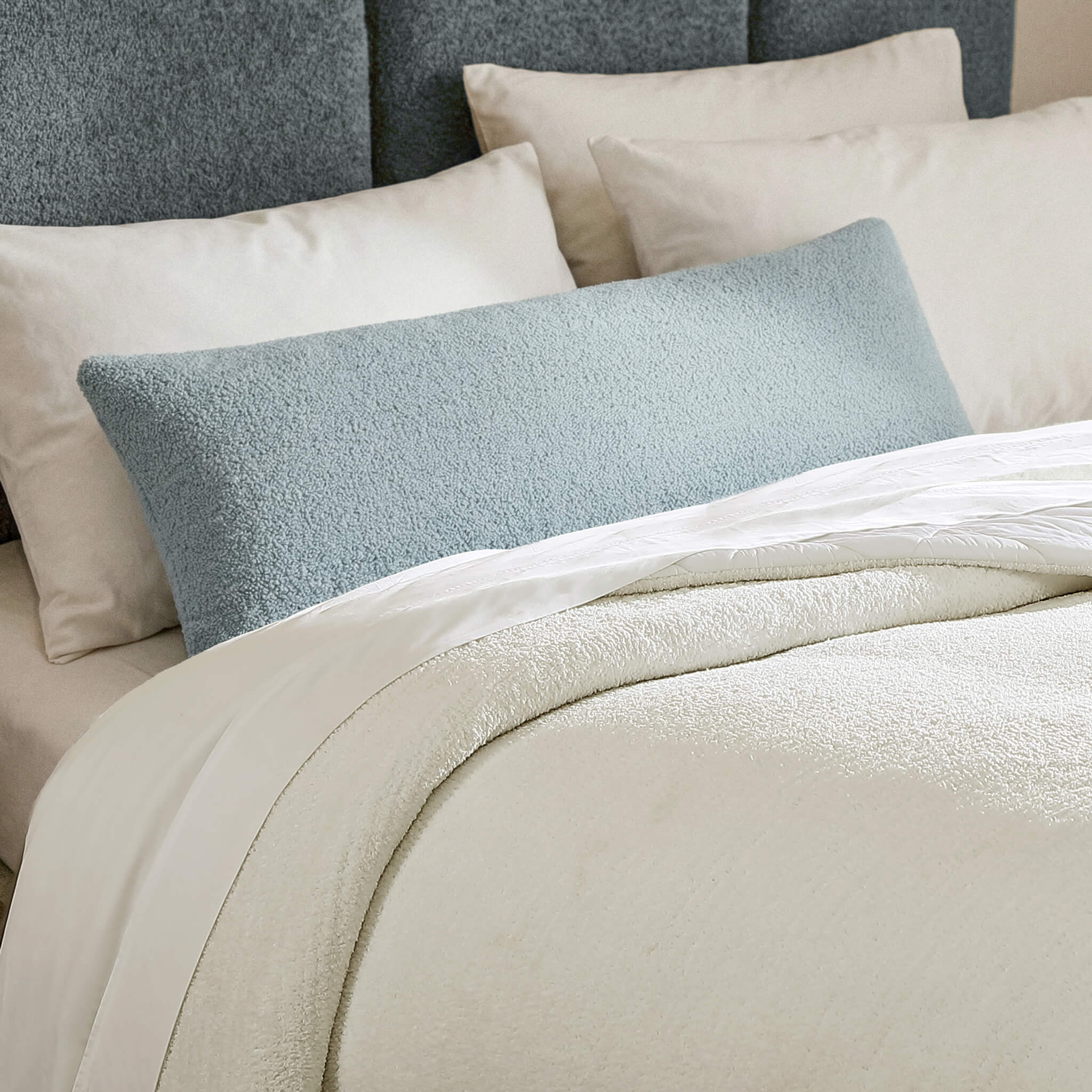 Neatly arranged pillows on a bed with a textured headboard Main image